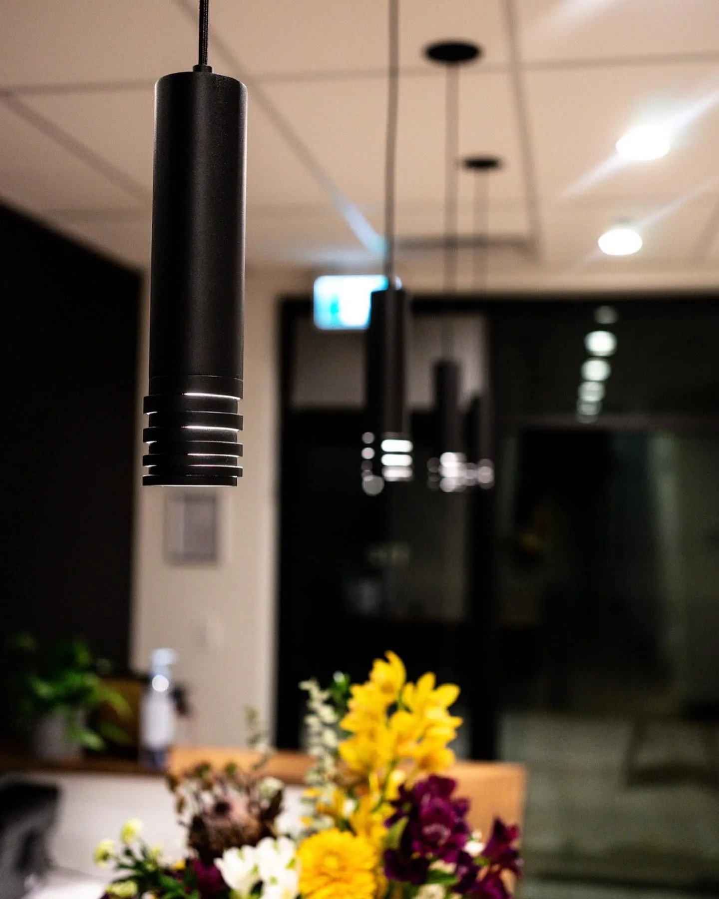 Black cylinder pendants hung in a finished commercial space with a glass partition behind.