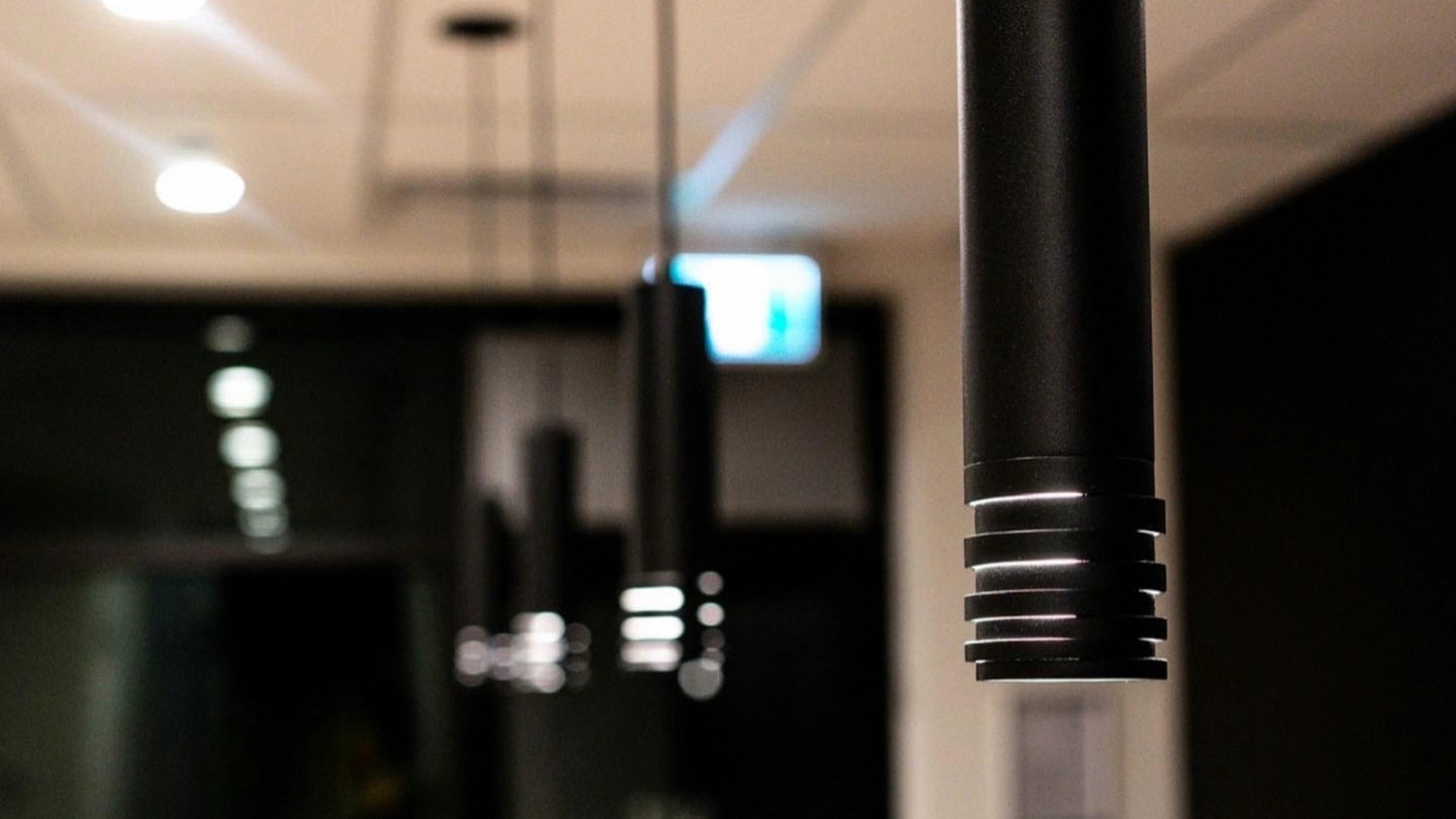Black cylinder pendants receding through a finished commercial space with a glass partition behind.