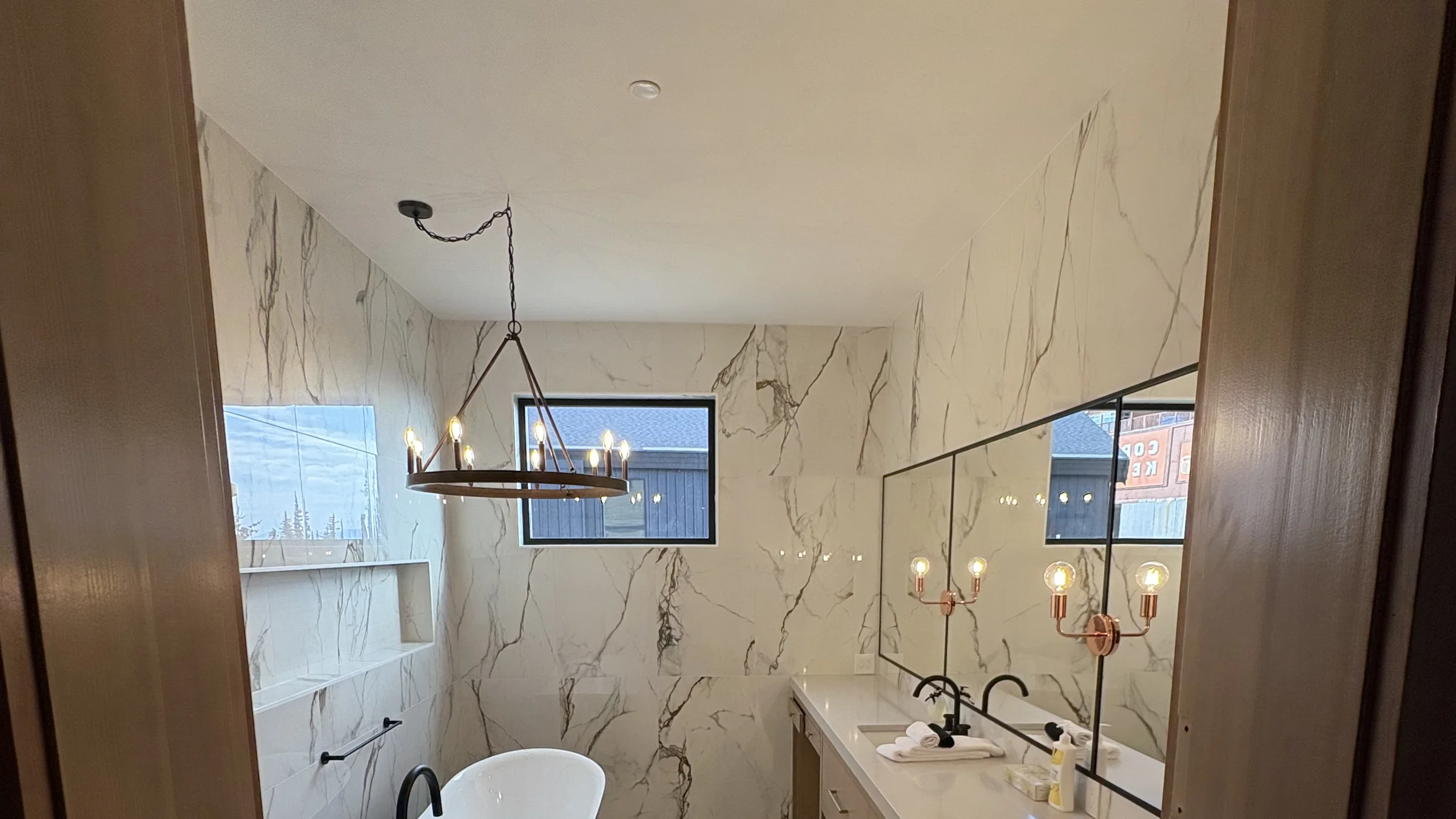 Marble ensuite lit by a wrought-iron chandelier and brass sconces in a custom Okanagan home.