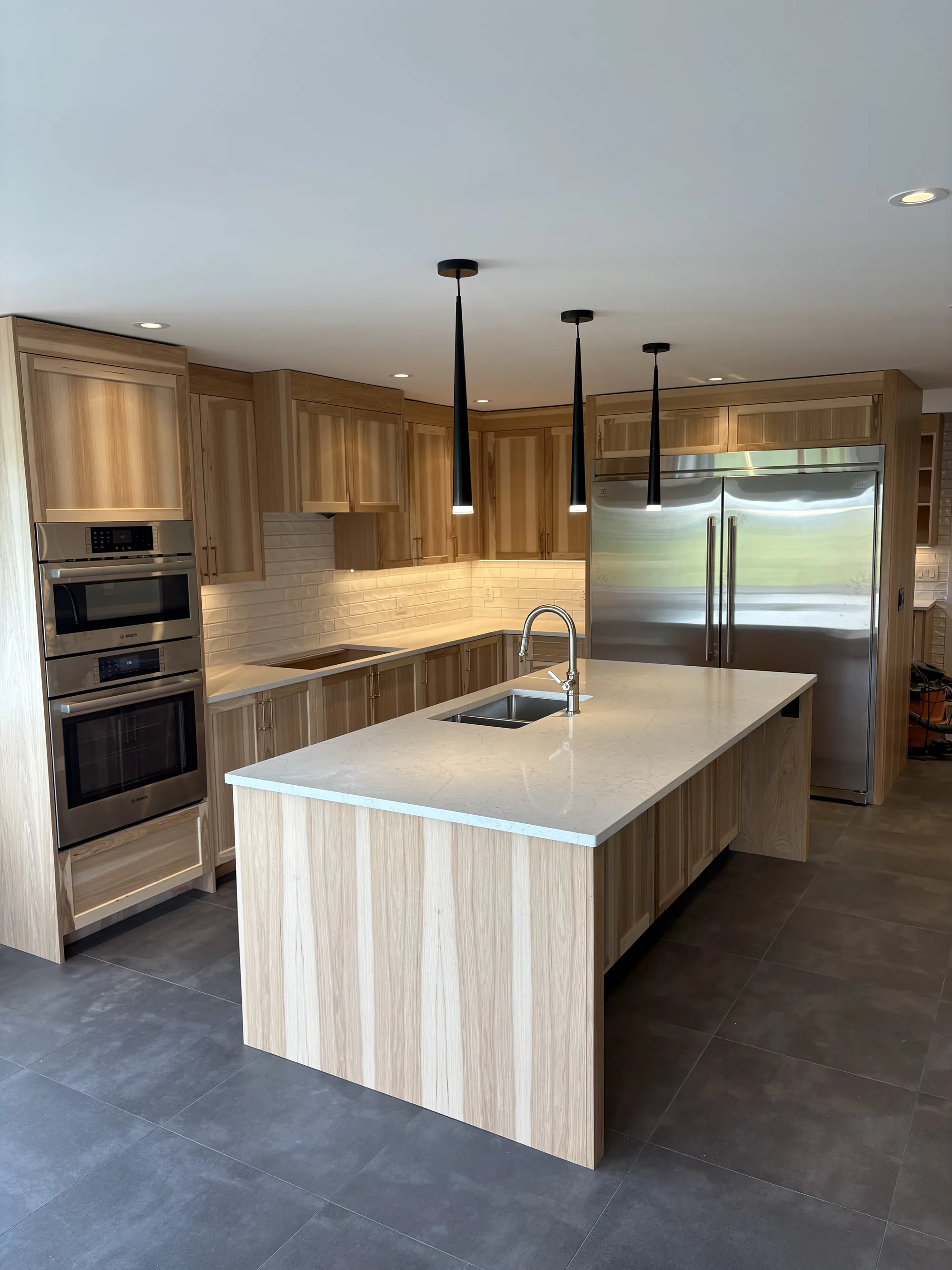 Finished custom kitchen in light oak with black cone pendants over the island and under-cabinet lighting.